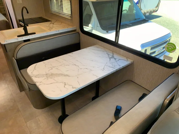 This RV rental offers a bright interior with a marble-look dinette, comfortable benches with seatbelts, and a kitchen area.. Coachmen Freelander 2022