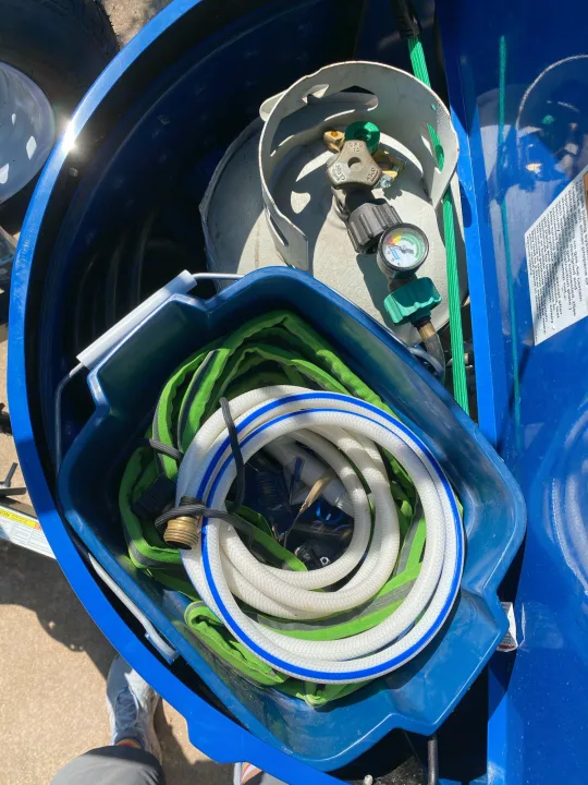 RV rental accessories: propane tank, water hose, and other gear stored in a blue bin, ready for a trip.. Little Guy NuCamp 2015