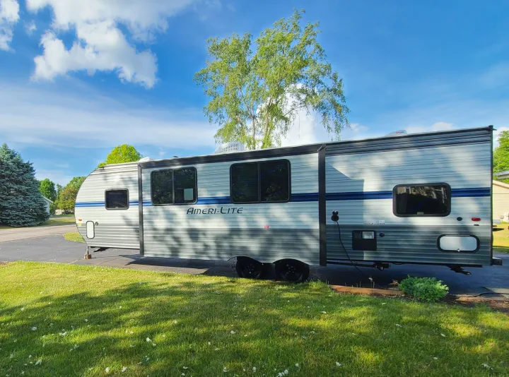 Light gray Ameri-Lite travel trailer, an excellent RV rental option, parked on a sunny lawn under a blue sky.. Gulf Stream Amerilite 2021