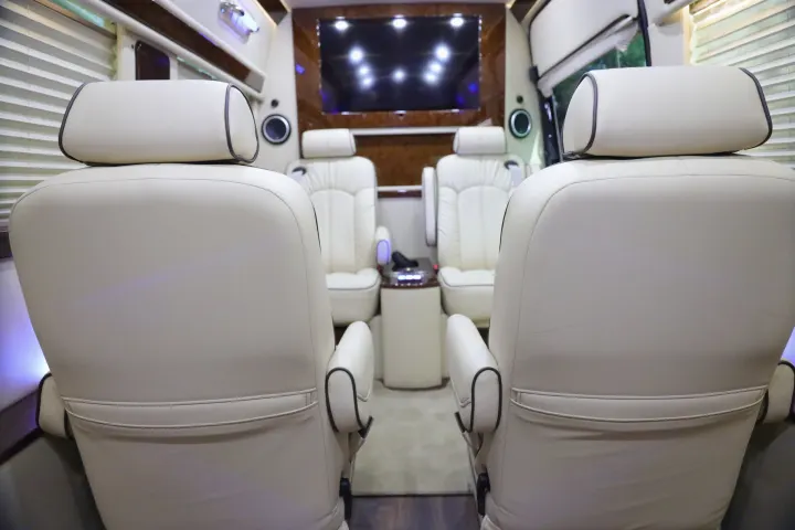 View of a luxurious RV rental interior, featuring cream captain's chairs and a large TV screen for ultimate comfort.. Mercedes 3500 2018