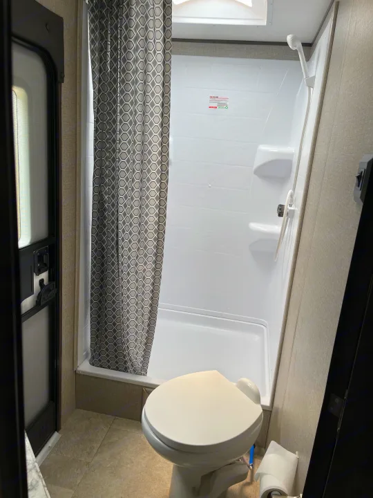 Clean and compact RV rental bathroom, featuring a white toilet, shower with patterned curtain, and tiled floor.. Jayco Jay Flight 2020