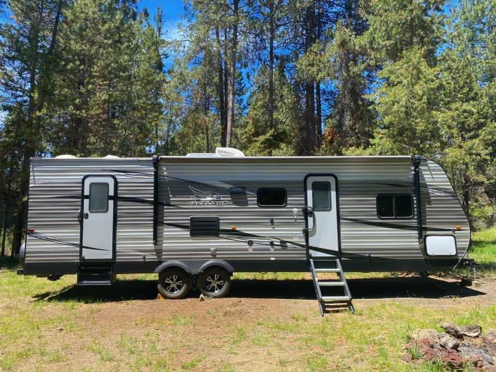 RV rental: A gray Jayco travel trailer parked amidst sunlit pine trees, ready for your outdoor camping adventure.. Jayco Jay Flight 2020