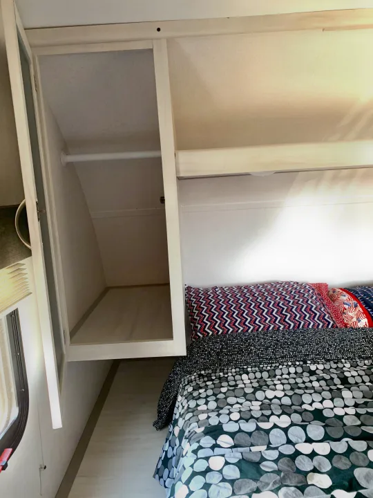 Compact RV rental bedroom featuring patterned bedding, open overhead storage, and a built-in closet.. Forest River Tracer 260BHSLE 2021