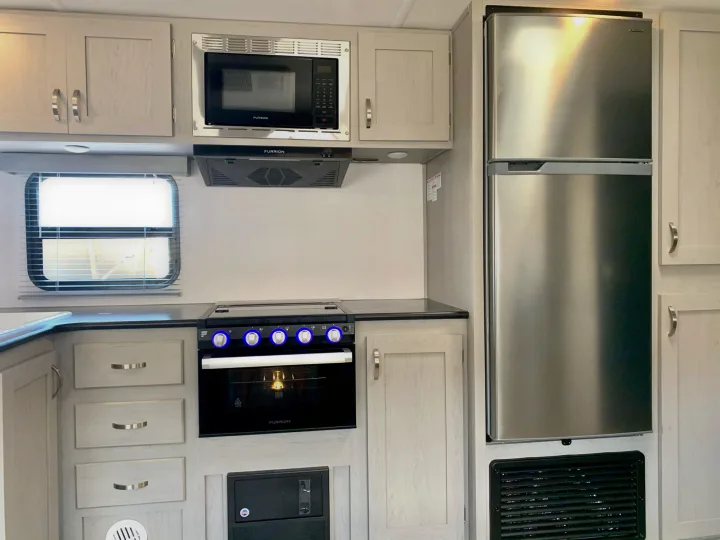 Compact RV rental kitchen with light cabinets, showcasing a microwave, stove, oven, and stainless steel refrigerator.. Forest River Tracer 260BHSLE 2021