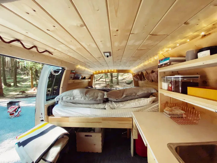 Inside a cozy RV rental: wood-clad camper van with comfy bed, compact kitchen, and scenic nature views. Ideal for adventure travel.. Chevrolet Express 2004
