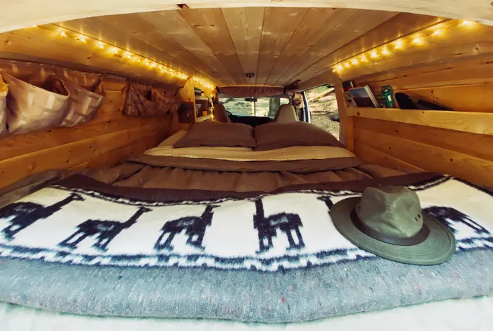 Cozy RV rental: wood-paneled camper van interior with string lights, bed, and travel essentials. Ready for adventure!. Chevrolet Express 2004