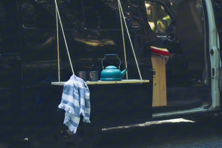 Cozy RV rental setup: hanging shelf with kettle, mugs, towel on black camper side. Perfect for outdoor adventure.. Chevrolet Express 2004