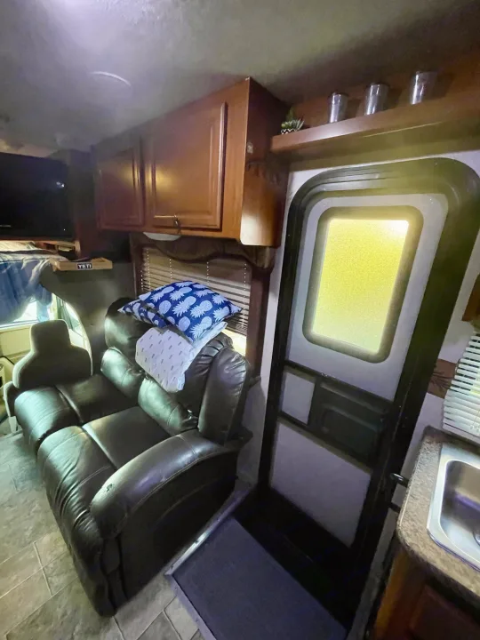 Spacious RV rental interior featuring a brown leather recliner sofa, overhead cabinets, and kitchen area.. Other Other 2010