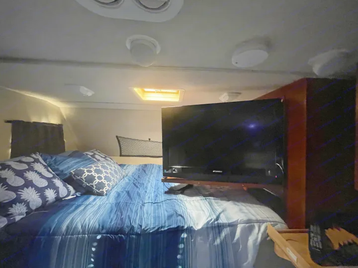 RV rental interior: cozy bedroom with blue bedding, a mounted TV, and ceiling skylight.. Other Other 2010