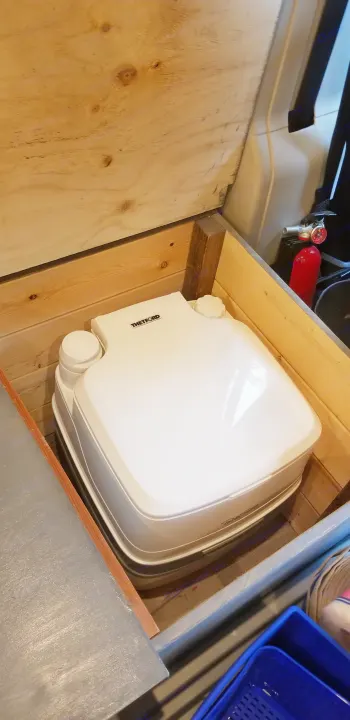 Compact Thetford portable toilet inside a custom wooden enclosure, ideal for an RV rental or camper van setup.. Dodge Ram Promaster 2500 2019