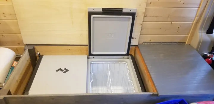 Compact RV rental living: A Dometic portable fridge with open lid in custom wooden storage, ideal for camper van adventures.. Dodge Ram Promaster 2500 2019