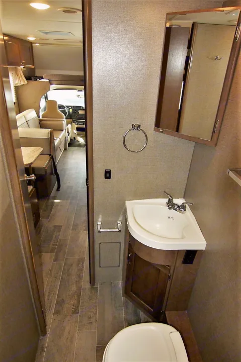 Compact RV rental interior: view from bathroom showing sink, toilet, and main living area with sofa & table. Ideal for travel.. Winnebago Outlook 2019