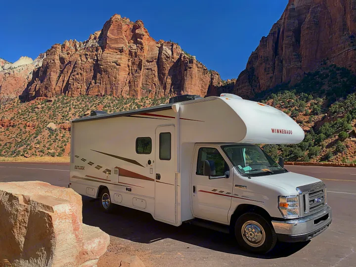 Winnebago RV rental parked before massive red sandstone mountains under clear blue skies at a national park.. Winnebago Outlook 2019