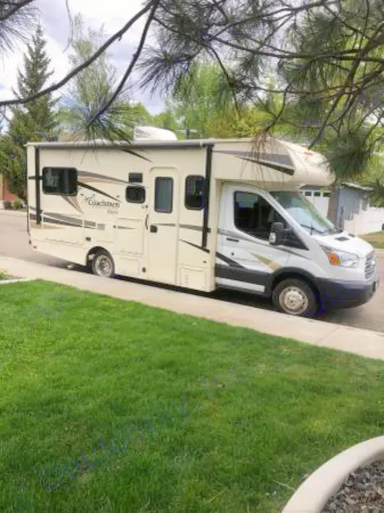 Side view of a white and beige Class C motorhome, ideal for RV rental adventures, parked curbside by green grass.. Coachmen Freelander 2018