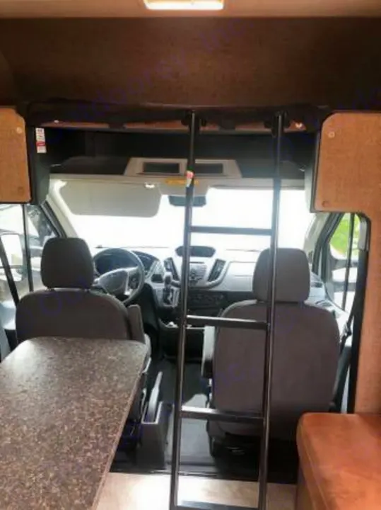 RV rental interior: Front cabin with driver/passenger seats, ladder to overhead bunk, and dining table on left.. Coachmen Freelander 2018