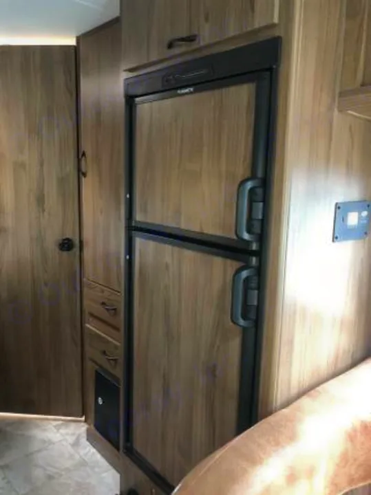 Inside your RV rental: a wood-paneled refrigerator/freezer and integrated cabinets provide compact, functional living.. Coachmen Freelander 2018