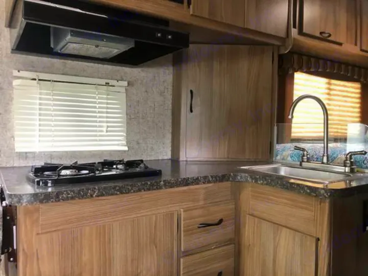 RV rental kitchen: compact interior with two-burner stove, sink, and light wood cabinets, perfect for travel.. Coachmen Freelander 2018