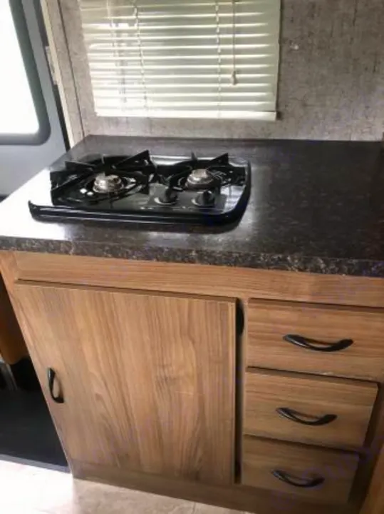 Compact kitchen in an RV rental featuring a two-burner stove, countertop, and wood-grain cabinets/drawers.. Coachmen Freelander 2018
