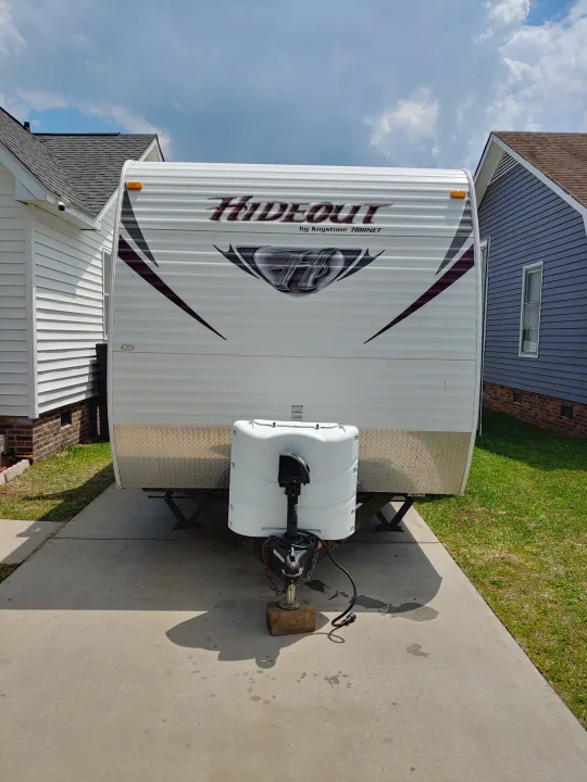 A white Hideout travel trailer/RV, parked in a driveway between houses. This travel trailer is ready for your rv rental adventure.. Keystone RV Hideout 2014