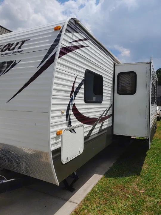 A bright white recreational vehicle (RV) travel trailer with extended slide-out, available for rv rental.. Keystone RV Hideout 2014
