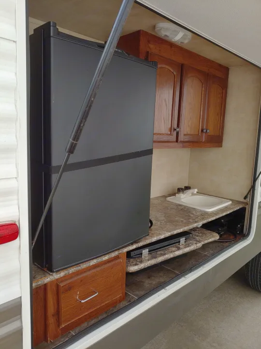 Outdoor kitchen setup in an RV rental, featuring a large black refrigerator, sink, and wooden cabinets for camping.. Keystone RV Hideout 2014