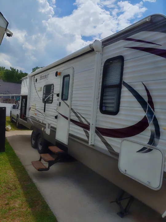 White RV rental travel trailer parked outdoors on a concrete pad, featuring an extended awning, steps, and side graphics.. Keystone RV Hideout 2014