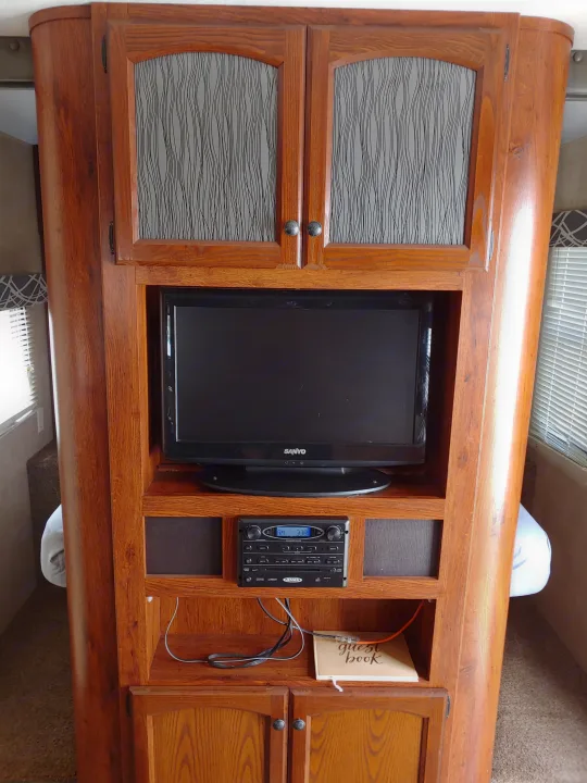 Inside an RV rental: a built-in wooden entertainment center featuring a Sanyo TV, Jensen stereo, & guest book.. Keystone RV Hideout 2014