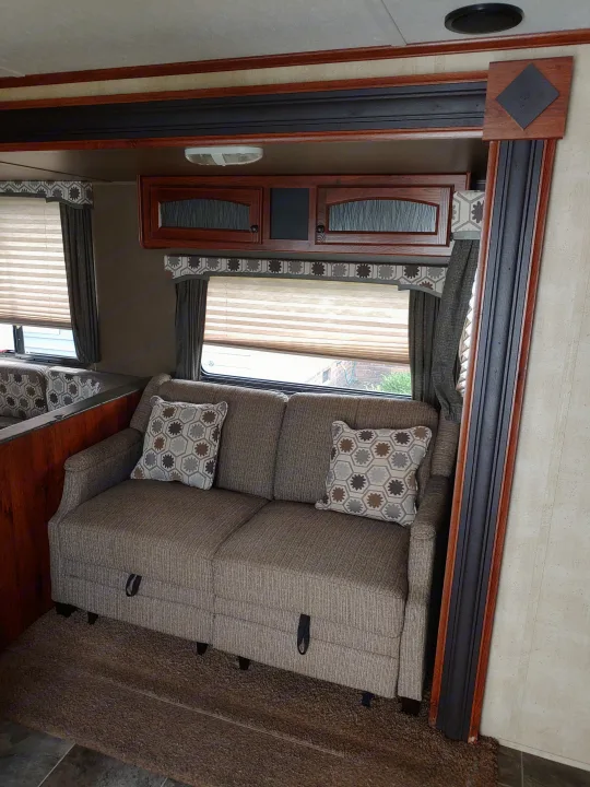 Comfortable RV rental living space featuring a sofa with decorative pillows, window blinds, and overhead cabinets.. Keystone RV Hideout 2014