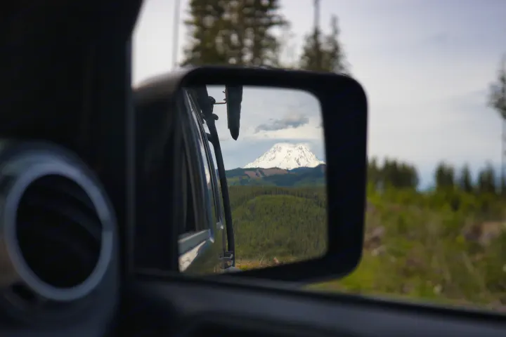 A snow-capped mountain vista and forest reflected in an RV rental's side mirror during a scenic road trip.. Jeep Wrangler Unlimited Rubicon 4x4 2013
