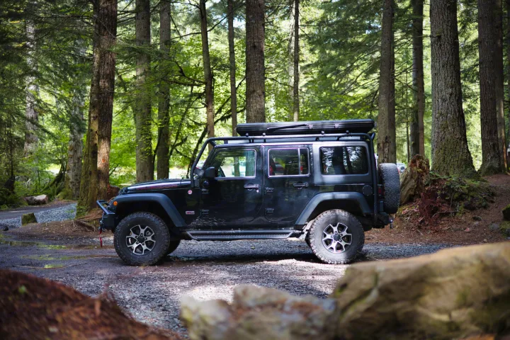 A black Jeep Wrangler with a rooftop tent is parked on a forest road.. Jeep Wrangler Unlimited Rubicon 4x4 2013