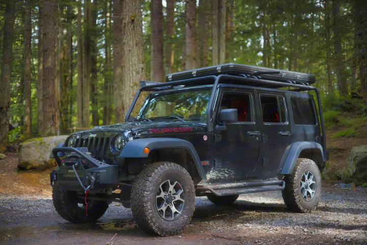 Rugged black Jeep Wrangler Rubicon with rooftop tent in a dense forest. Perfect for an adventure or rv rental.. Jeep Wrangler Unlimited Rubicon 4x4 2013