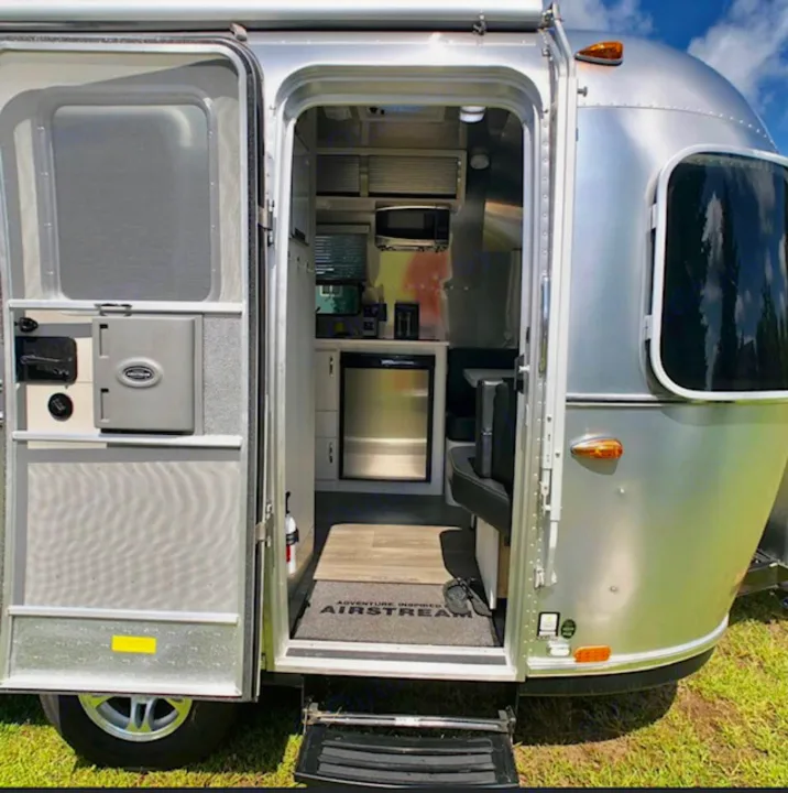 Step inside this Airstream travel trailer RV rental. Its open door reveals a compact kitchen with a fridge & microwave.. Airstream Sport 2018