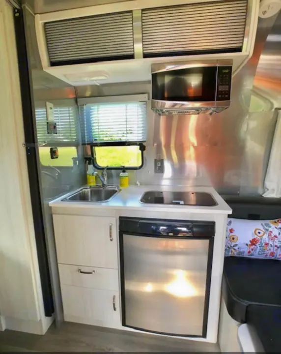 Modern RV rental kitchen with stainless steel appliances: sink, cooktop, microwave, fridge, and overhead storage. Ready for adventure!. Airstream Sport 2018