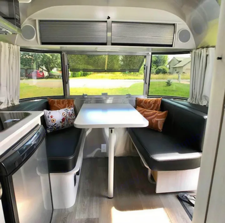 RV rental interior shows a bright Airstream dinette with black benches, a white table, and large windows looking out.. Airstream Sport 2018