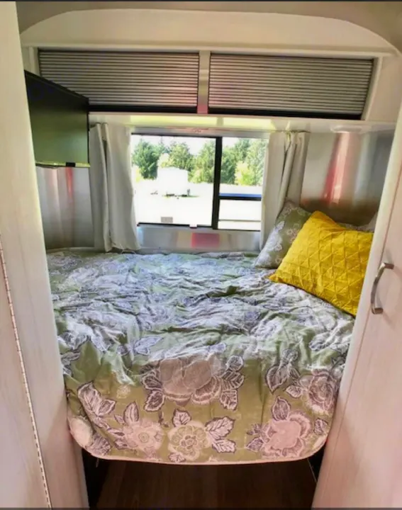 Cozy RV rental bedroom with a floral bedspread, TV, and large window. Perfect for travel adventures.. Airstream Sport 2018