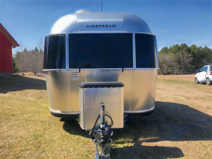 Front view of an Airstream rv rental: a shiny silver travel trailer parked on a grassy field with a red building nearby.. Airstream Sport 2018