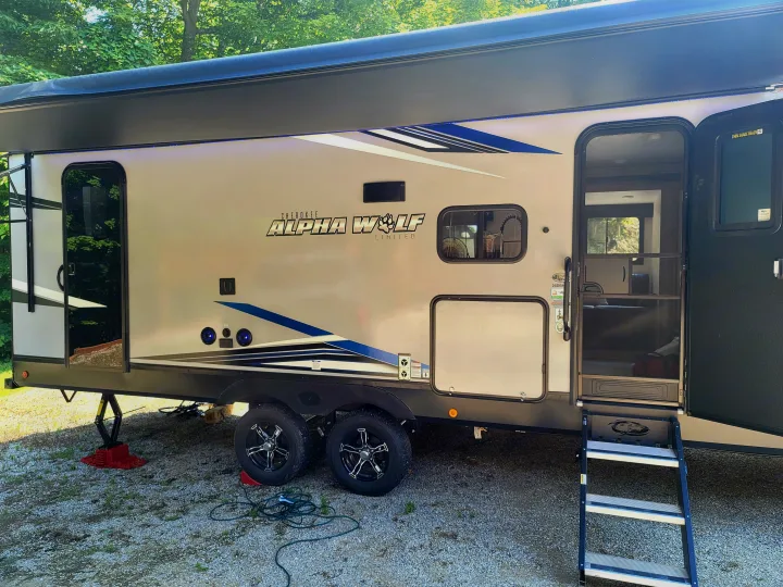 Ready for adventure: this Alpha Wolf travel trailer RV rental is parked with its awning and steps extended at a sunny campsite.. Forest River Cherokee Alpha Wolf 2021