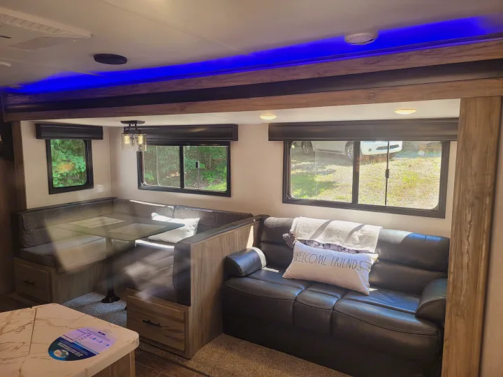 Cozy RV rental interior with dinette, couch, large windows, and blue overhead accent lighting. Ideal for road trips.. Forest River Cherokee Alpha Wolf 2021
