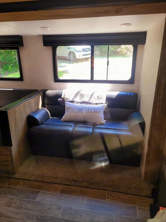 Inside an RV rental: a comfy dark sofa, "Welcome Friends" pillow, and scenic window views from this inviting living space.. Forest River Cherokee Alpha Wolf 2021