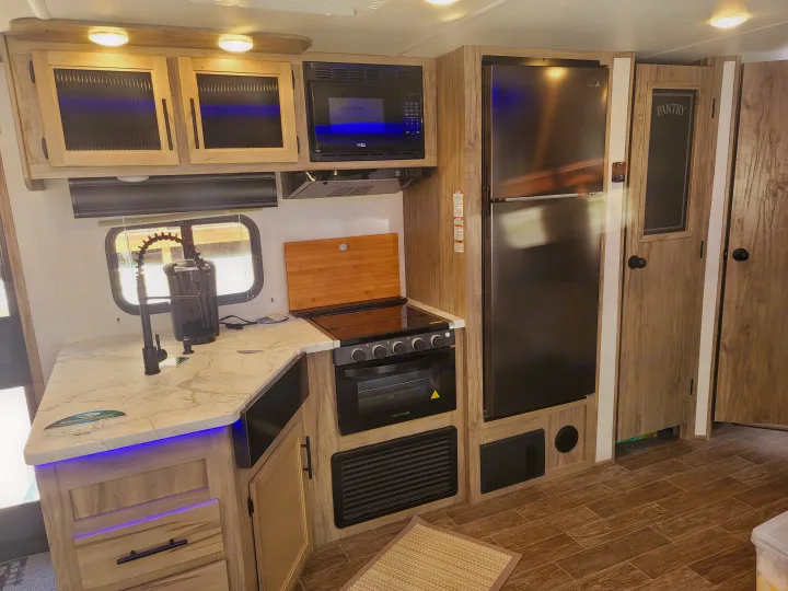 Modern RV rental kitchen featuring a refrigerator, microwave, stove, and stylish sink setup. Ready for culinary adventures!. Forest River Cherokee Alpha Wolf 2021