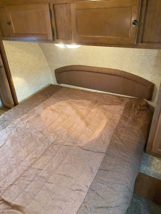 Inside an RV rental bedroom: brown quilted bed, wood cabinets, and textured walls.. Skyline NOMAD Joey Select 292 BHS  Double Wide Bunk 2014