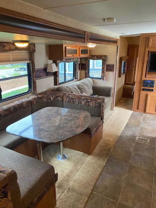 RV rental interior: living/dining area with patterned sofas, a table, windows, and wood cabinets. A cozy space for your travels.. Skyline NOMAD Joey Select 292 BHS  Double Wide Bunk 2014