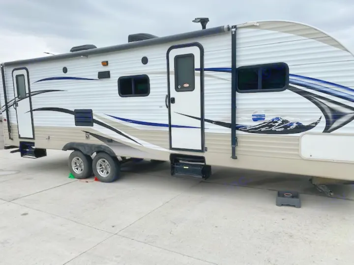 Side view of a white and tan travel trailer RV rental, with blue mountain graphics, parked on concrete. Ideal for your next trip.. Skyline NOMAD Joey Select 292 BHS  Double Wide Bunk 2014