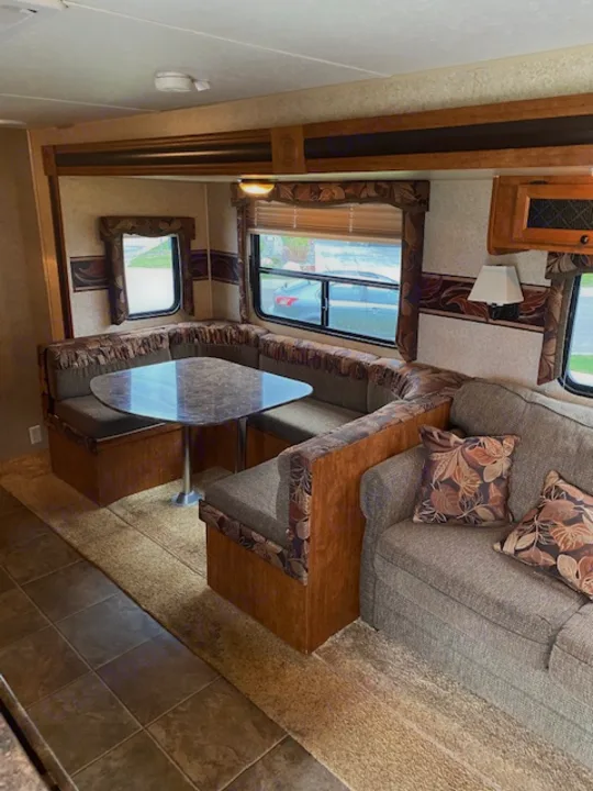 Cozy rv rental interior featuring a gray sofa, U-shaped dinette with a glass table, and windows. Perfect for travel adventures.. Skyline NOMAD Joey Select 292 BHS  Double Wide Bunk 2014