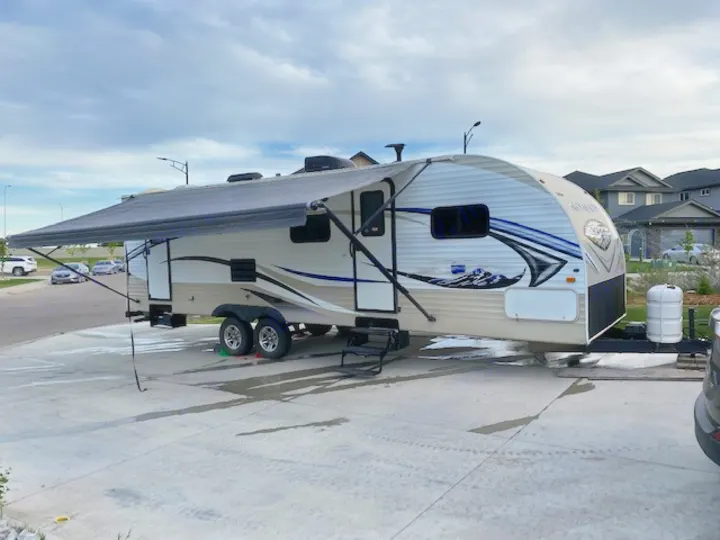 A white travel trailer with a mountain graphic, often an RV rental, parked on a driveway with its awning extended.. Skyline NOMAD Joey Select 292 BHS  Double Wide Bunk 2014