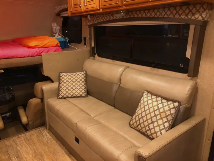Inviting RV rental living space with a comfy bunk bed, plush leather sofa, and wood cabinets, offering cozy comfort.. Thor Chateau 2017