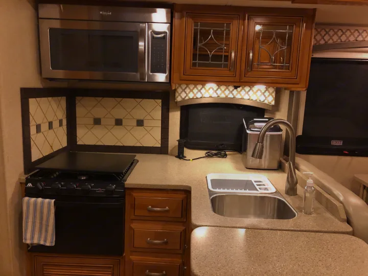 Inside an RV rental kitchen, featuring a microwave, gas stove, sink, cabinets, and an emergency exit sign on the window.. Thor Chateau 2017
