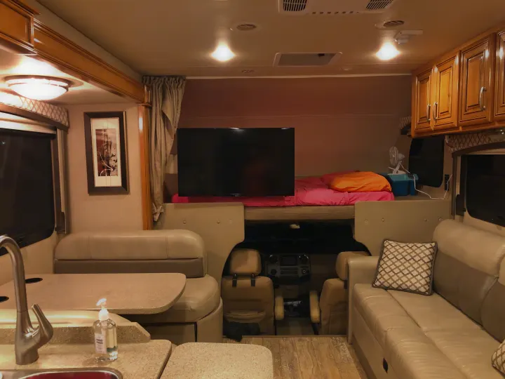 Spacious RV rental interior featuring a living area, kitchen, and cab-over bunk with a TV and bed.. Thor Chateau 2017