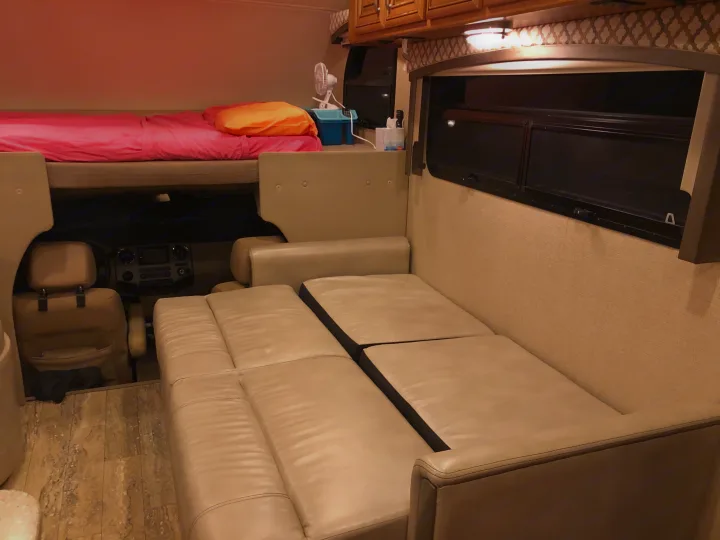 Experience comfort in this RV rental interior, featuring a bunk bed, driver's area, and a versatile couch for seating or sleeping.. Thor Chateau 2017