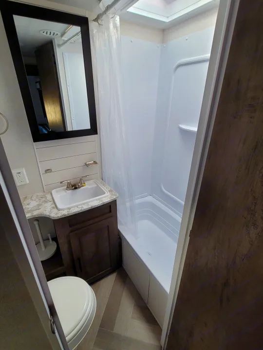 Compact RV rental bathroom features a shower with curtain, sink vanity, toilet, and modern flooring.. Forest River Salem 2021